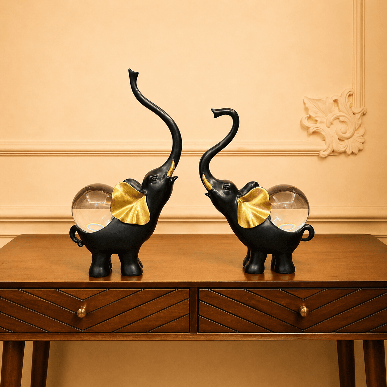 Pair of black elephant statues with golden ears and clear crystal balls on their backs, displayed on a wooden entryway console table