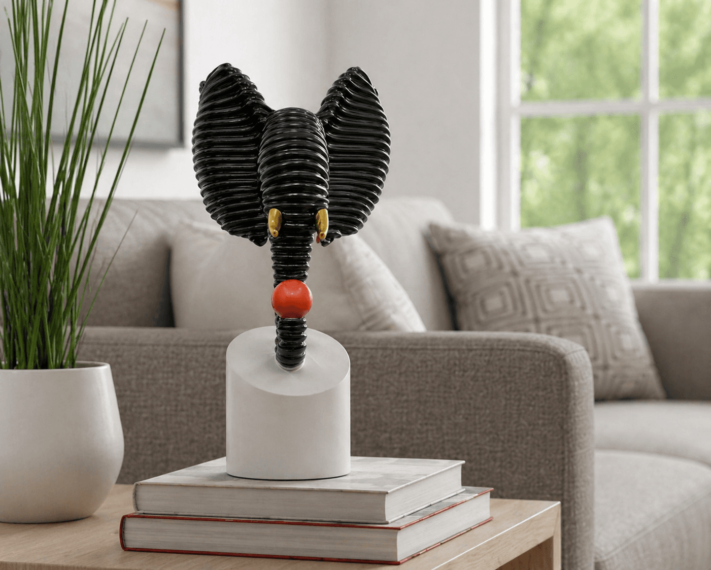 Abstract black textured elephant head sculpture holding a red ball, displayed on a modern living room side table over decorative books