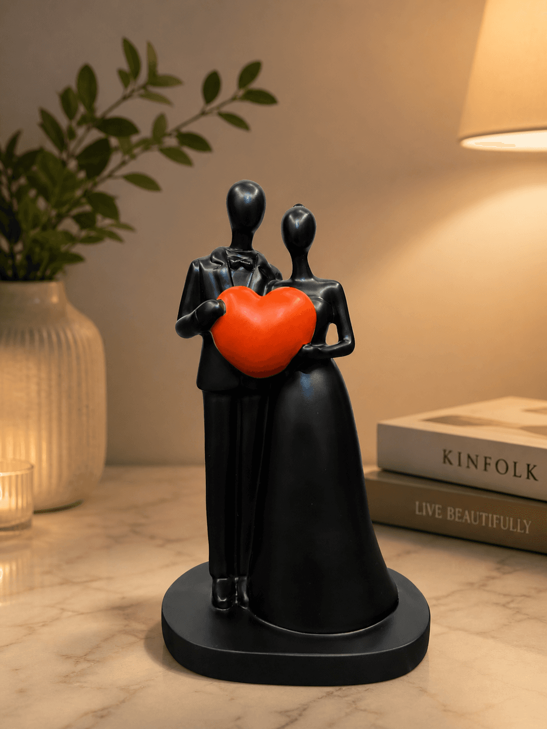 Modern black abstract sculpture of a couple holding a bright red heart, placed on a marble table with candles for romantic bedroom decor