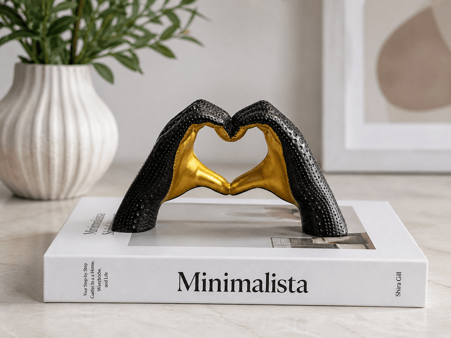 Modern black and gold textured sculpture of hands forming a heart shape, displayed on coffee table books for elegant home decor