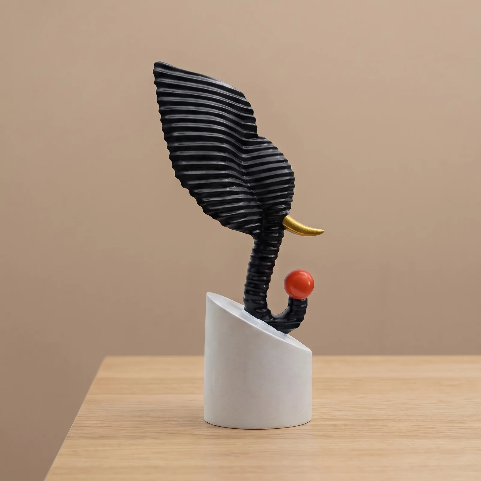 Abstract black textured elephant head sculpture holding a red ball, displayed on a modern living room side table over decorative books preview 2